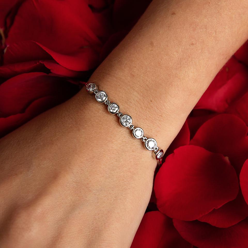Photo of a models wrist wearing a white gold diamond bezel set bracelet on a bed of rose petals 