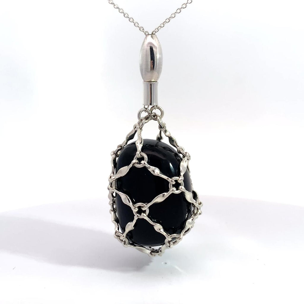 photo of a silver lattice encased black onyx pendant on a long chain on a white background