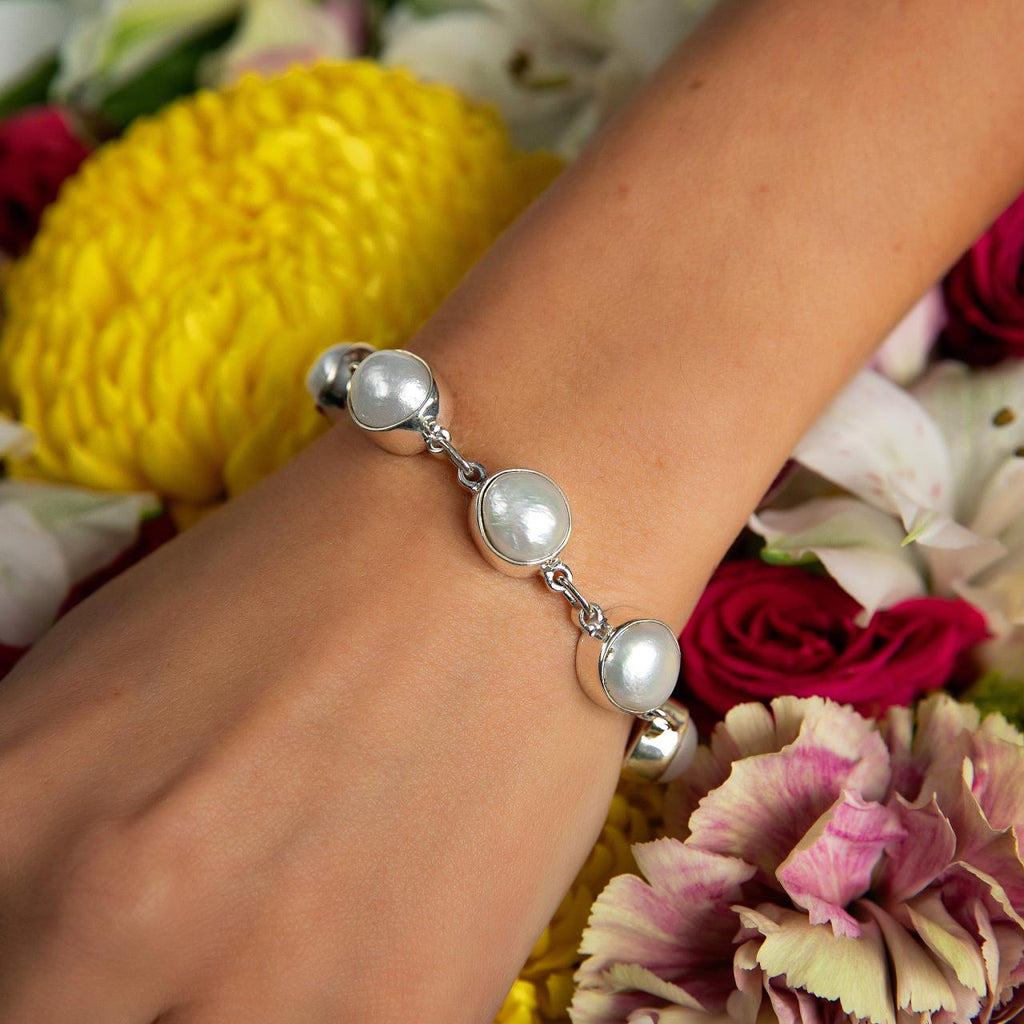 photo of a models arm wearing a silver white pearls bracelet on a bed of flowers 