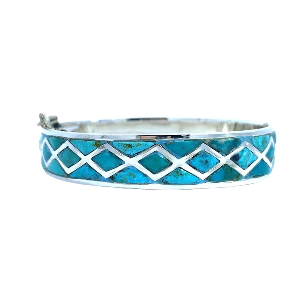photo of a silver bangle with turquoise inlaid in a repeating diamond pattern on a white background
