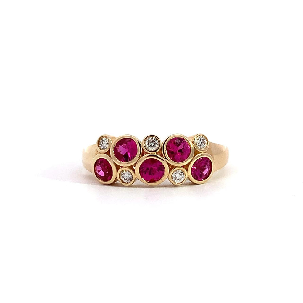 photo of a ring with bezel set round pink sapphires and diamonds in yellow gold on a white background 