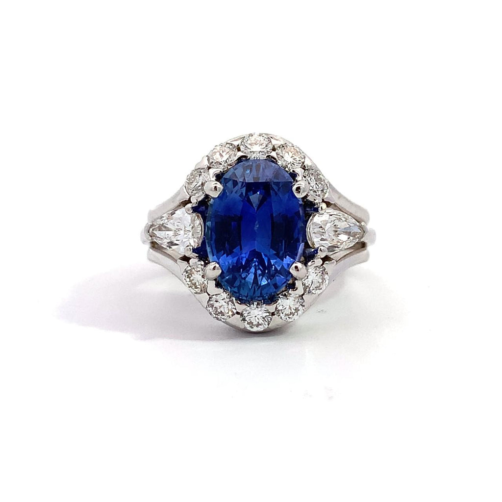 photo of a white gold ring oval blue sapphire with a diamond halo and pear-shaped diamond sides on a white background