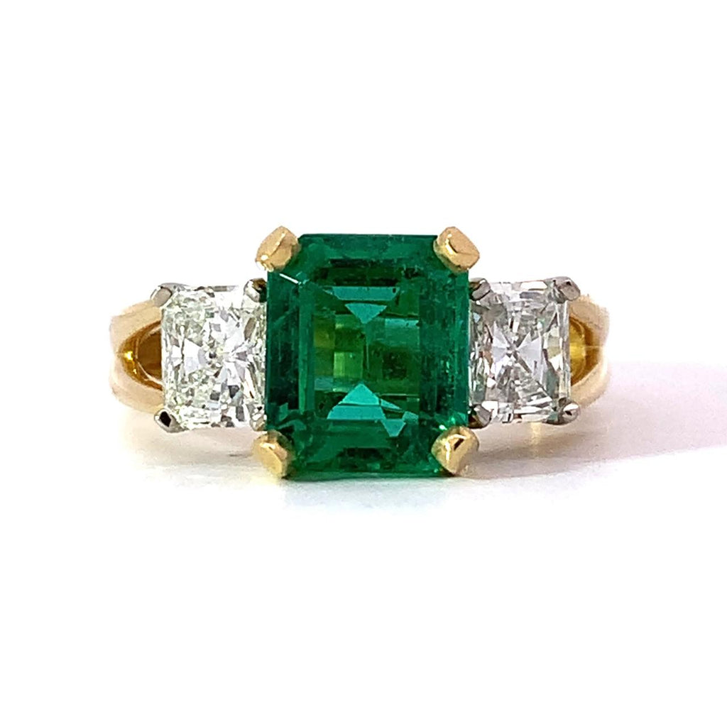 photo of a 18kyg ring with a center emerald cut emerald flanked by radiant cut diamonds on a white background