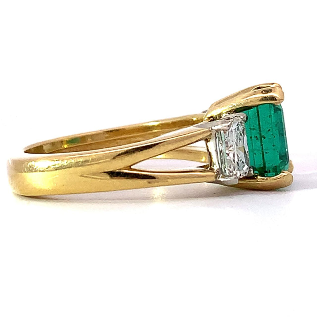 photo of a 18kyg ring with a center emerald cut emerald flanked by radiant cut diamonds on a white background side view 